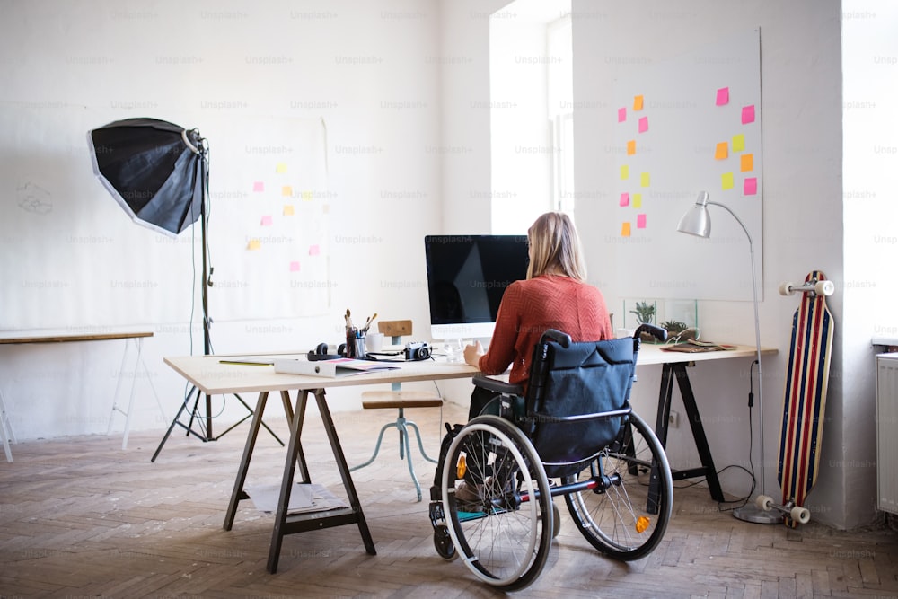 Femme d’affaires en fauteuil roulant assise au bureau, travaillant. Vue arrière.