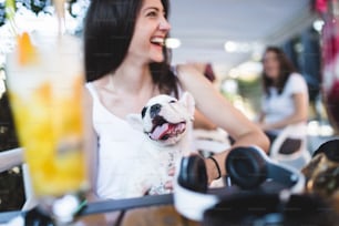 Schöne junge Frau sitzt im Café mit ihrem entzückenden französischen Bulldoggenwelpen. Frühlings- oder Sommerstadt im Freien. Menschen mit Hunden Thema.
