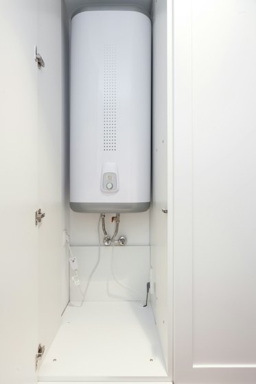 Wall-mounted tank water heater with supply lines in a utility closet
