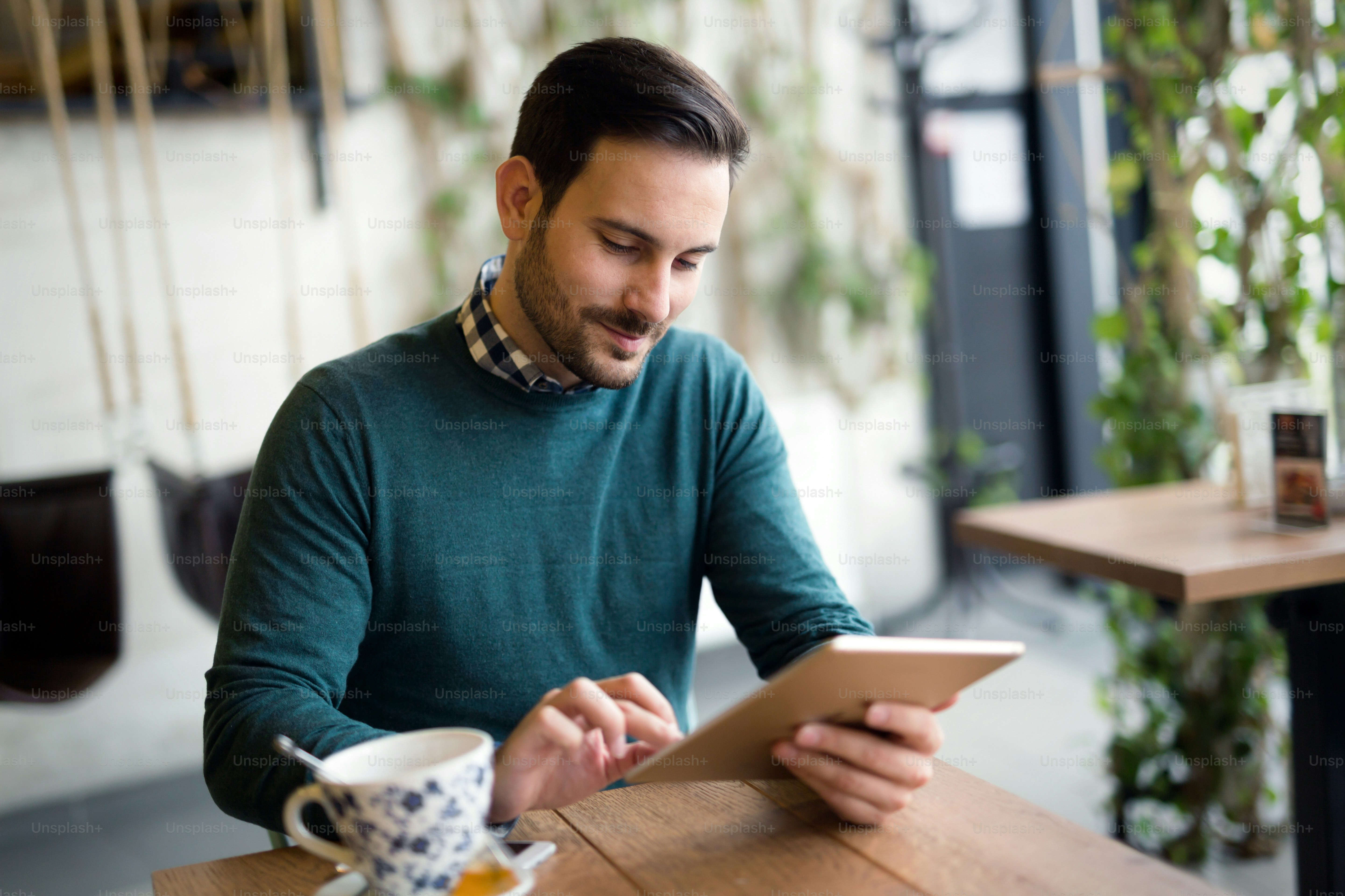 Handsome young man smiling and holding tablet computer in coffee shop