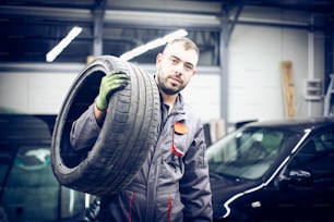 Young man at workshop carrying tires. Portrait.