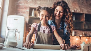 Attractive young woman and her little cute daughter are cooking on kitchen. Having fun together while making cakes and cookies.
