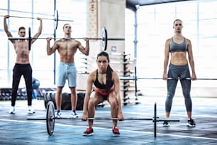 Un grupo de deportistas musculosos se ejercita en el gimnasio. Entrenamiento en el gimnasio. Hombres guapos sin camisa y mujeres atractivas están haciendo ejercicios con pesas. Halterofilia.