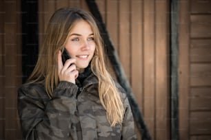 portrait Young beautiful woman in winter in the snow using mobile phone