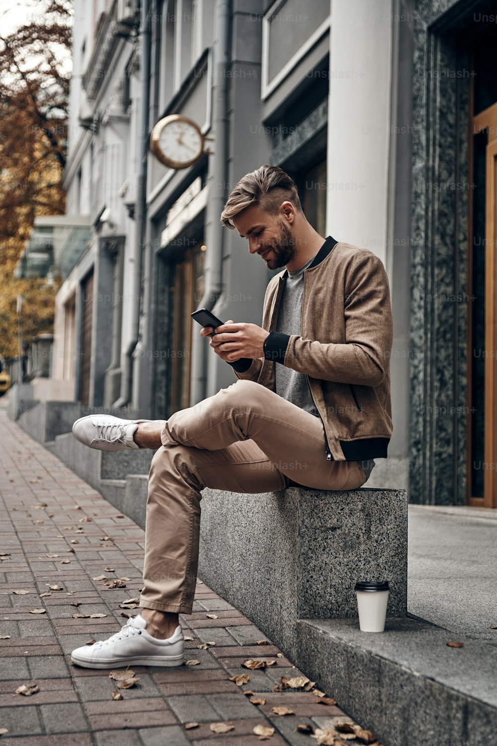Hübscher junger Mann in Freizeitkleidung, der sein Smartphone benutzt, während er draußen sitzt