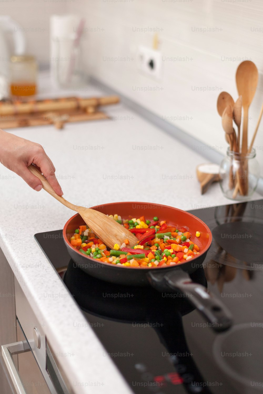 Vegetables are in a frying pan. Woman cooking colourful fresh vegetables on an electric stove