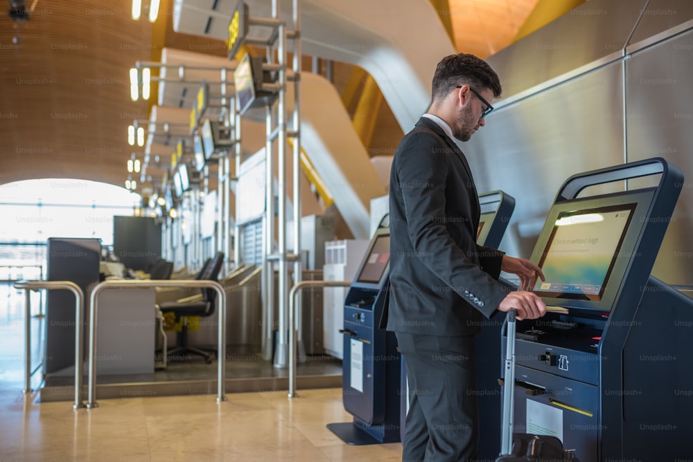 Jeune homme d’affaires faisant l’auto-enregistrement dans une machine à l’aéroport