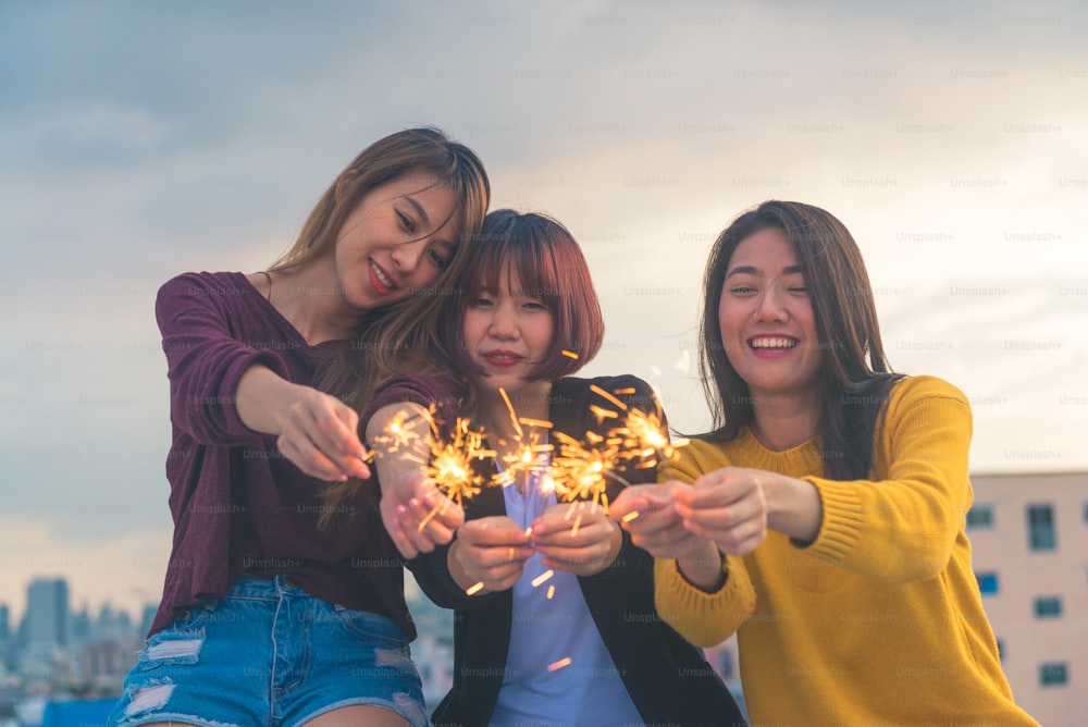 Outdoor shot of young people at rooftop party. Happy group of asia girl friends enjoy and play sparkler at roof top party at evening sunset. Holiday celebration festive party. Teenage lifestyle party.