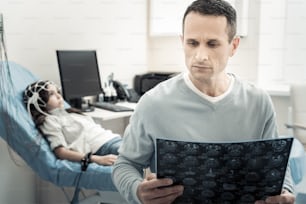 Magnetic scanning. Serious nice handsome man holding an X ray scan and studying it while worrying about his child