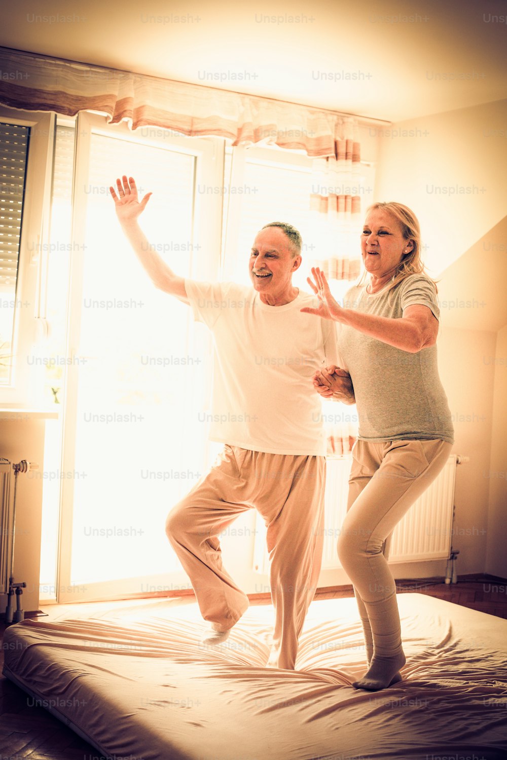 Senior couple  jumping together on bed and having fun.