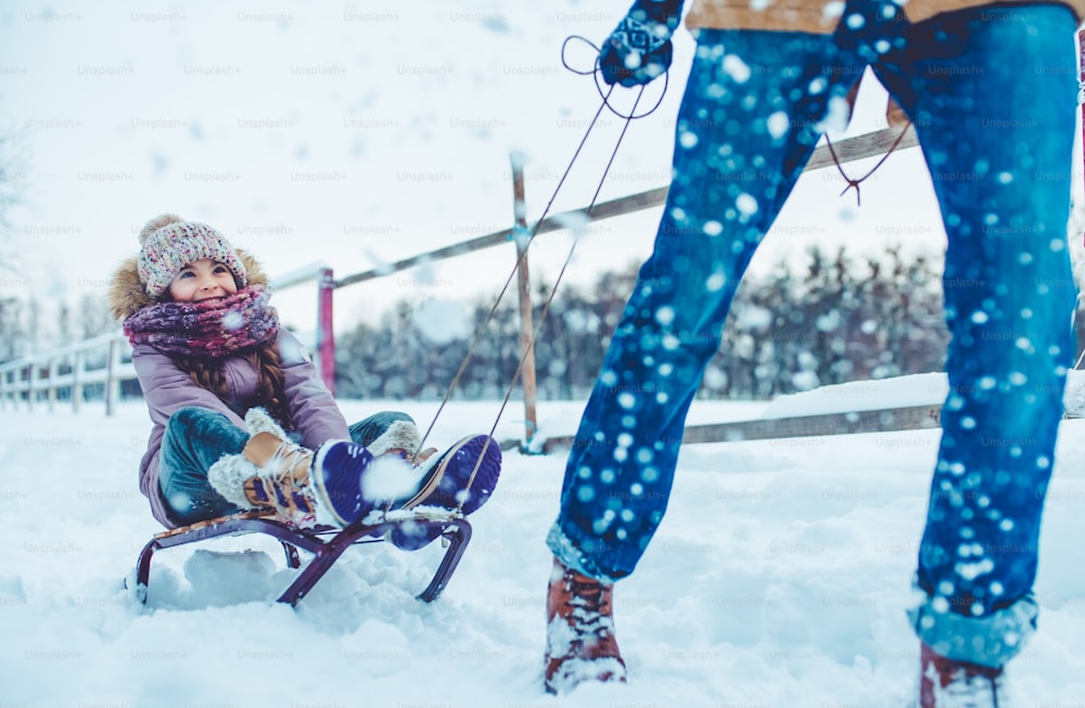 Der gutaussehende junge Vater und seine kleine süße Tochter haben im Winter Spaß im Freien. Genießen Sie es, Zeit miteinander zu verbringen, während Sie auf einem Schlitten fahren. Familienkonzept.