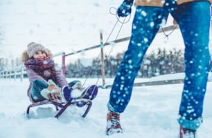 Un joven y guapo padre y su pequeña y linda hija se divierten al aire libre en invierno. Disfrutar de pasar tiempo juntos mientras montamos en un trineo. Concepto de familia.