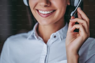 ご用件は何ですか。ヘッドフォンを着けた魅力的な女性コールセンターワーカーが微笑んでいるトリミングされた画像。