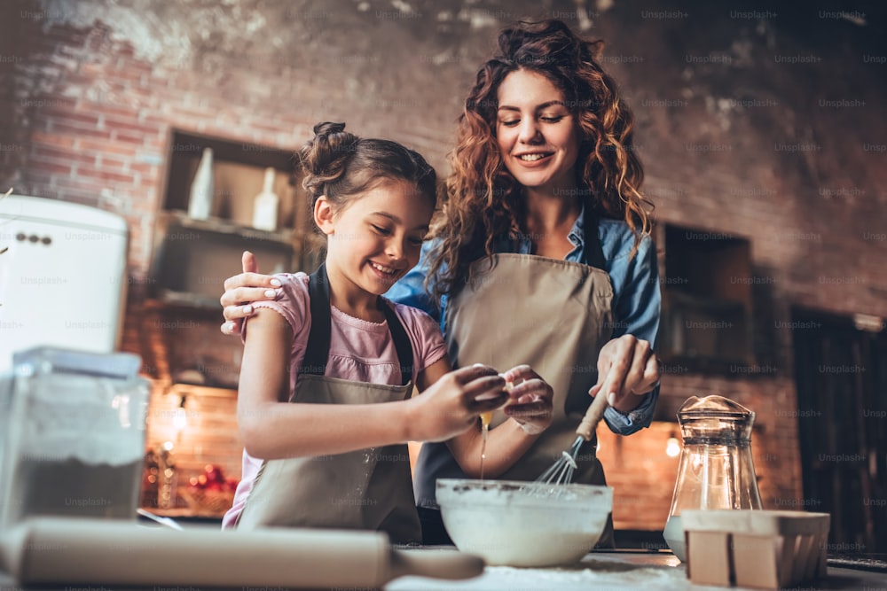Giovane donna attraente e la sua piccola figlia carina stanno cucinando in cucina. Divertirsi insieme mentre si preparano torte e biscotti.