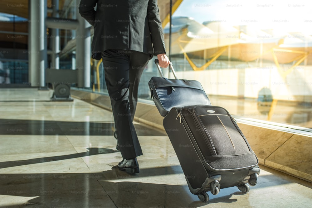 Schiena e gambe dell'uomo d'affari che camminano con i bagagli all'aeroporto