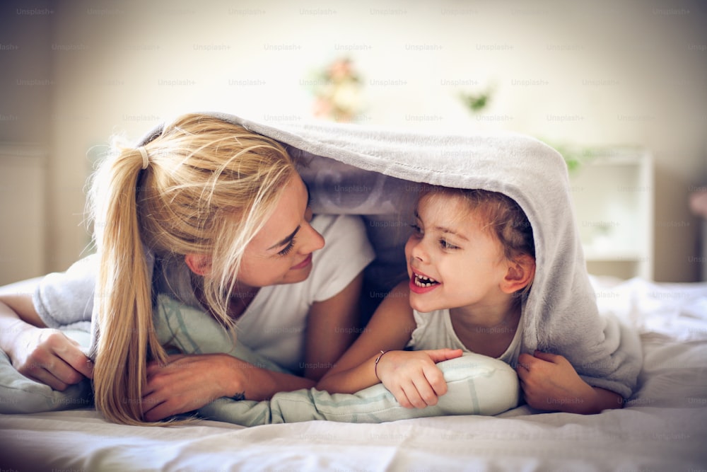 Mãe e filha debaixo do cobertor pela manhã.