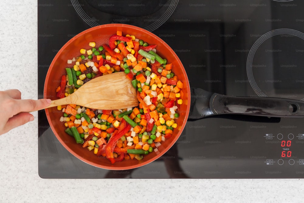 Vegetables are in a frying pan. Woman cooking colourful fresh vegetables on an electric stove