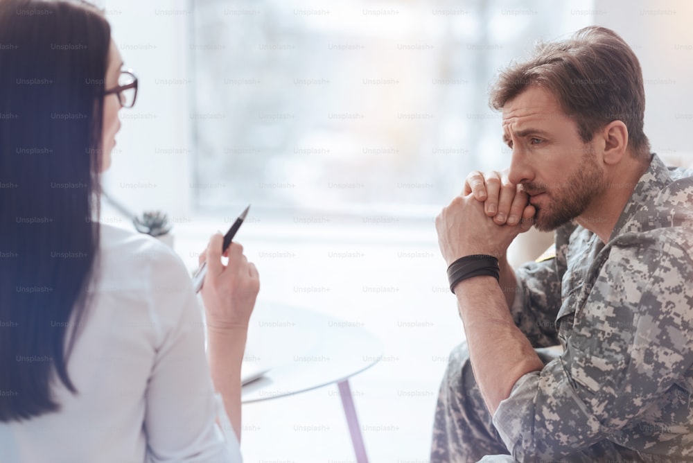 Trauma mental de la posguerra. Un militar sentado en un sofá y escuchando a una terapeuta profesional que le da consejos y trata de ayudarle a seguir con su vida.