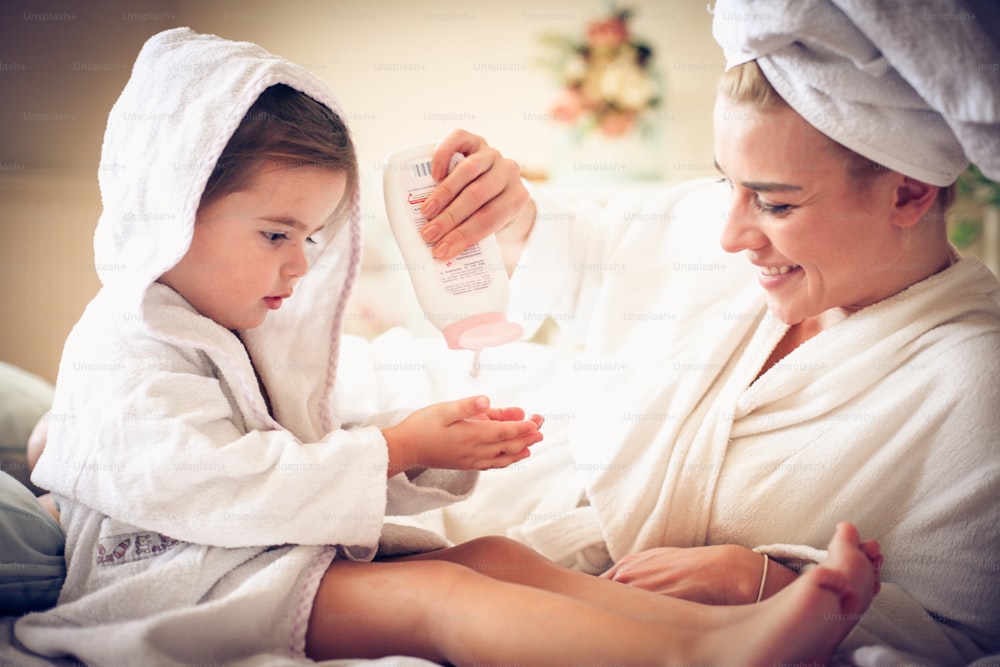 Portrait of mother and daughter after bath applying body lotion.