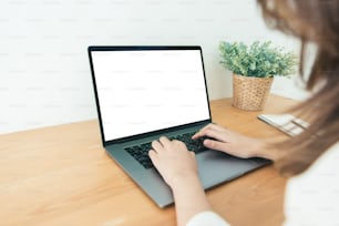 Jeune femme asiatique travaillant à l’aide et tapant sur un ordinateur portable avec une maquette d’écran blanc vierge à la maison dans un espace de travail de bureau. Femme d’affaires travaillant à domicile via un ordinateur portable. Profiter du temps passé à la maison.