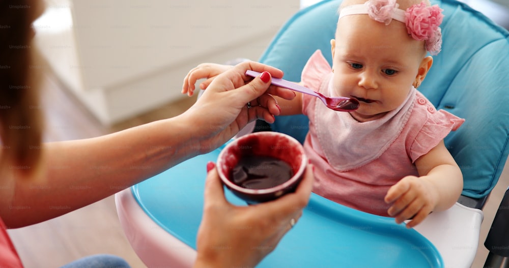 Mother feeding baby girl with spoon indoors