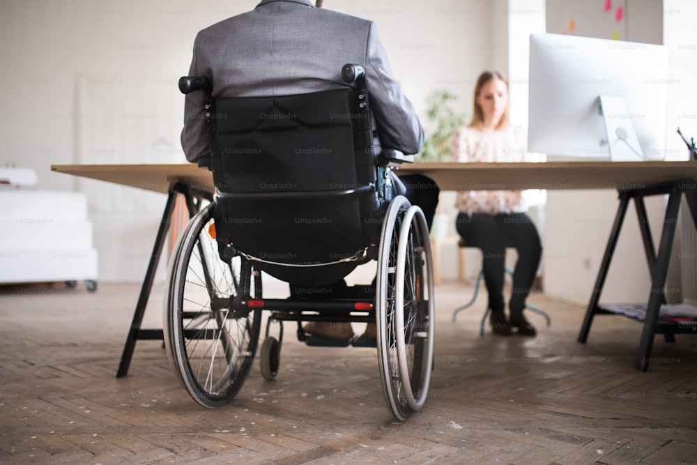 Due uomini d'affari irriconoscibili con sedia a rotelle in ufficio che lavorano insieme.