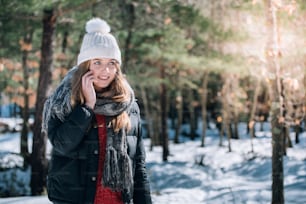 携帯電話を使用して雪の中の冬の肖像画若い美しい女性