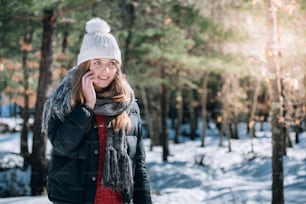 portrait Young beautiful woman in winter in the snow using mobile phone