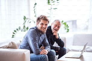 Hipster son and his senior father at home. Two generations indoors, having fun.Hipster son with his senior father at home. Two generations indoors, having fun.