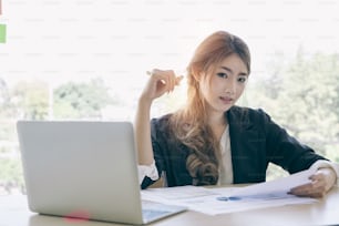 Attractive asian young businesswoman working on laptop while be smile in her workstation at desk with bright window in background