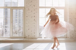Süßes kleines Mädchen in wunderschönem Kleid tanzt im hellen, sonnigen Raum