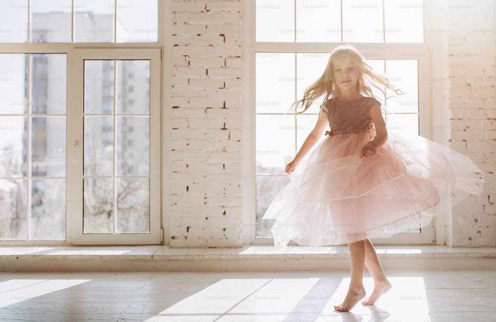 Cute little girl in beautiful dress is dancing at light sunny room