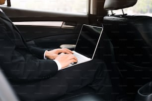 Businessman using computer working car inside.