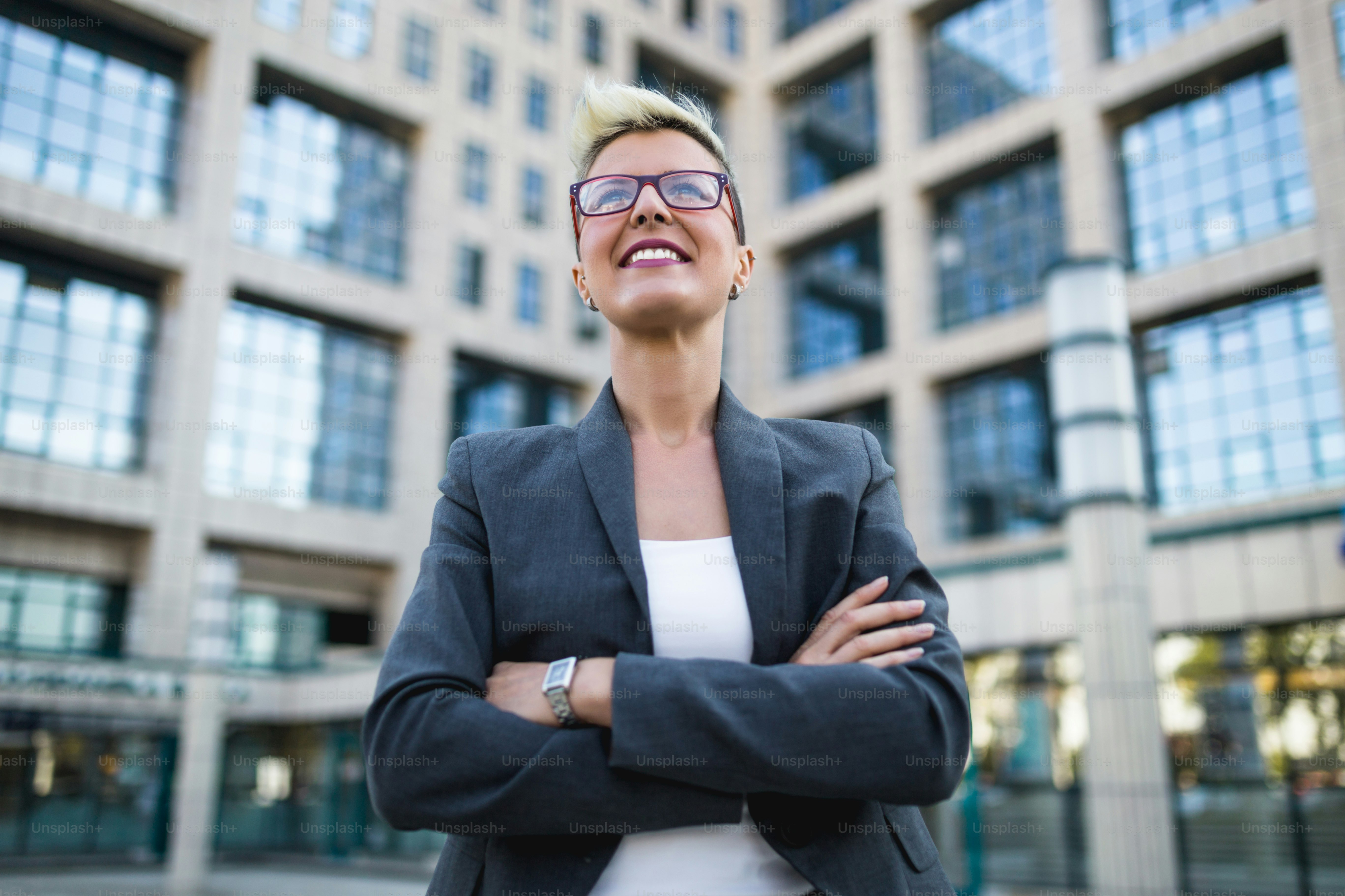 Jeune femme d’affaires heureuse debout devant un grand bâtiment moderne. Elle sourit et parle sur son téléphone portable.