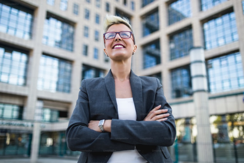 Young happy business woman standing in front of big modern building. She smiling and talking on her cell phone.