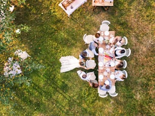 Réception de mariage à l’extérieur dans la cour arrière. Les mariés avec une famille debout autour de la table, saluant. Vue aérienne.