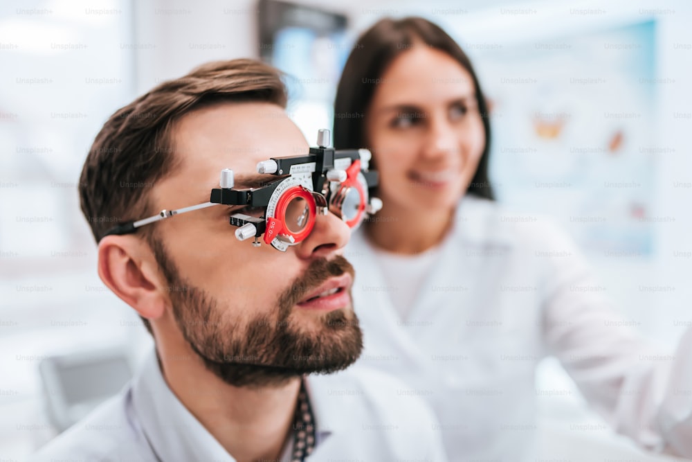 L'attraente medico oftalmologo sta controllando la visione degli occhi di un bel giovane nella clinica moderna. Medico e paziente in clinica oftalmologica.