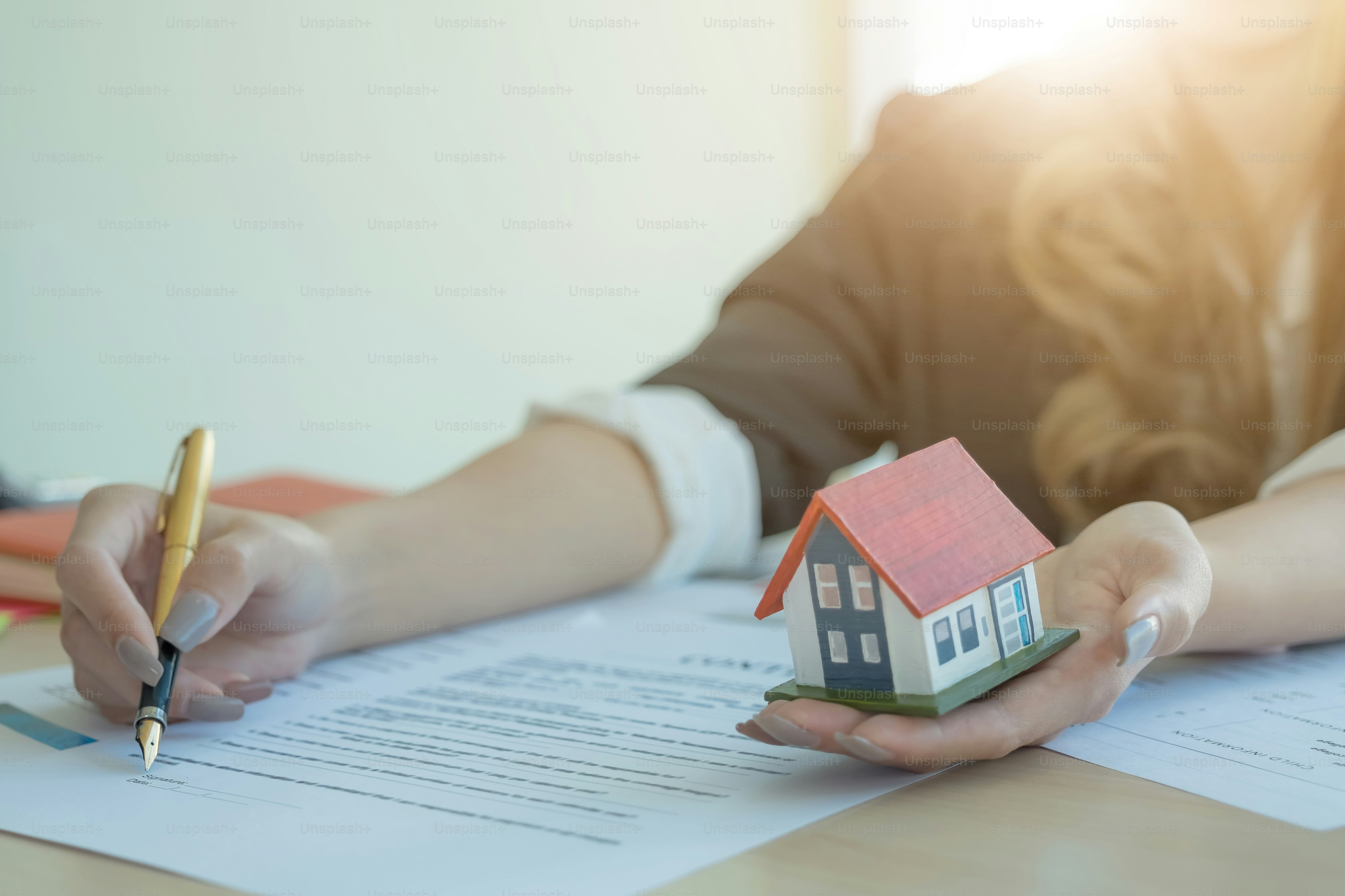 A businesswoman signing a paper with house miniature in hand