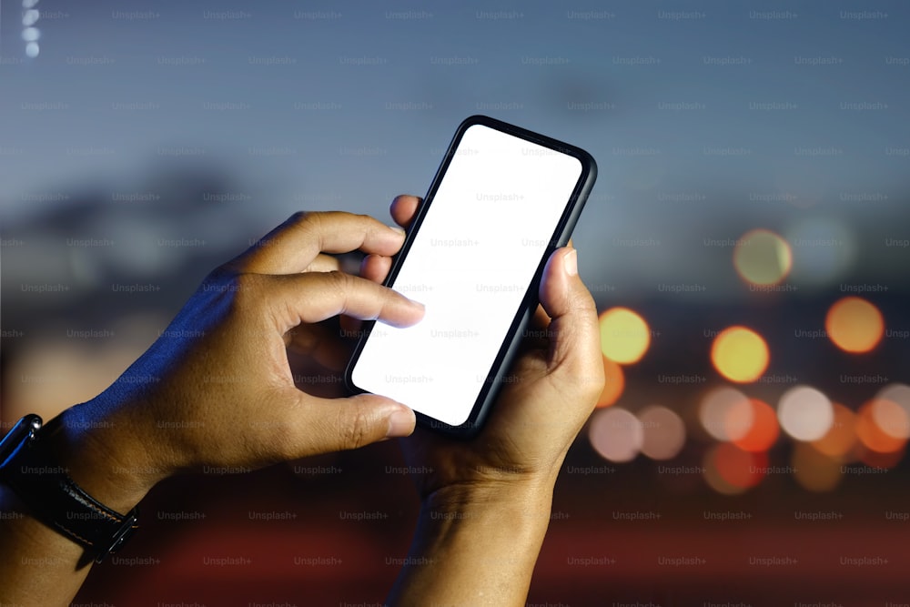 Closeup of male hands showing blank screen smartphone outside, bokeh lights