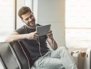 Porträt eines fröhlichen bärtigen Mannes, der Lied hört, während er auf ein elektronisches Tablet schaut. Zufriedener Mann ruht mit Gadget-Konzept