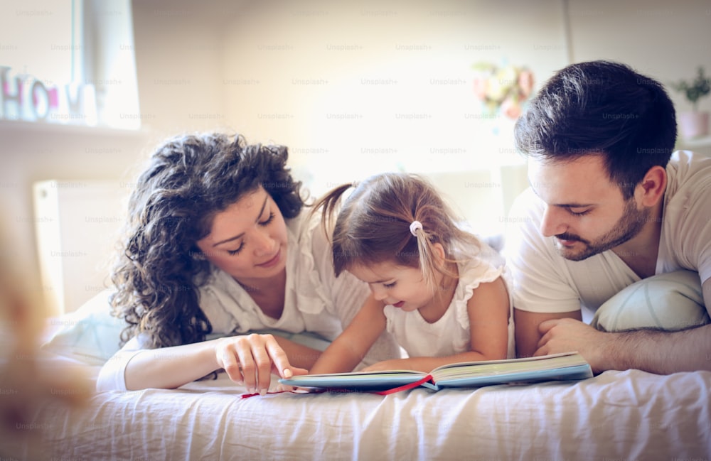 Young parents with their little girl looking color book. Morning routine.