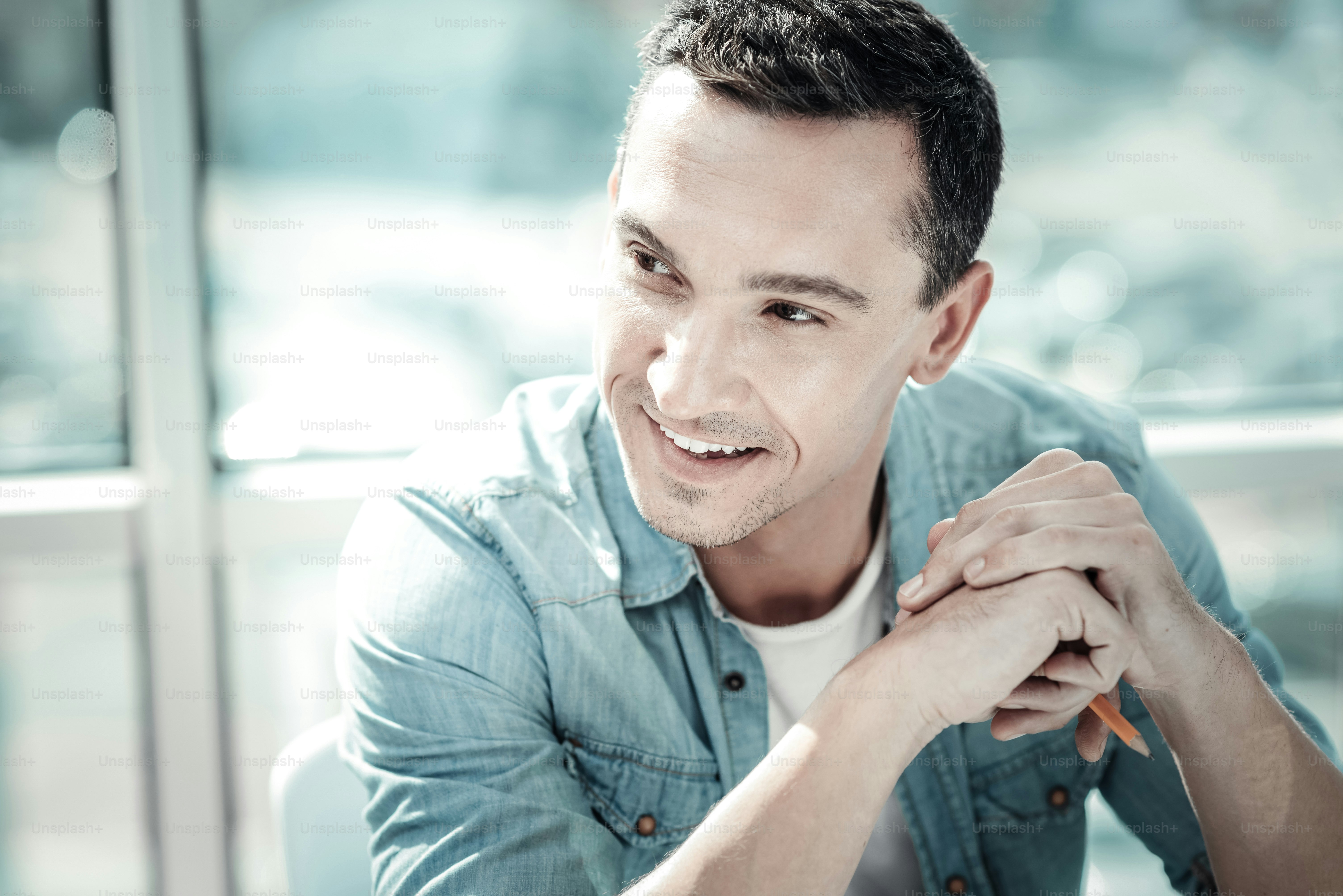 Im listening to you. Pleasant attentive responsible man sitting in the bright room holding a pencil and looking aside.