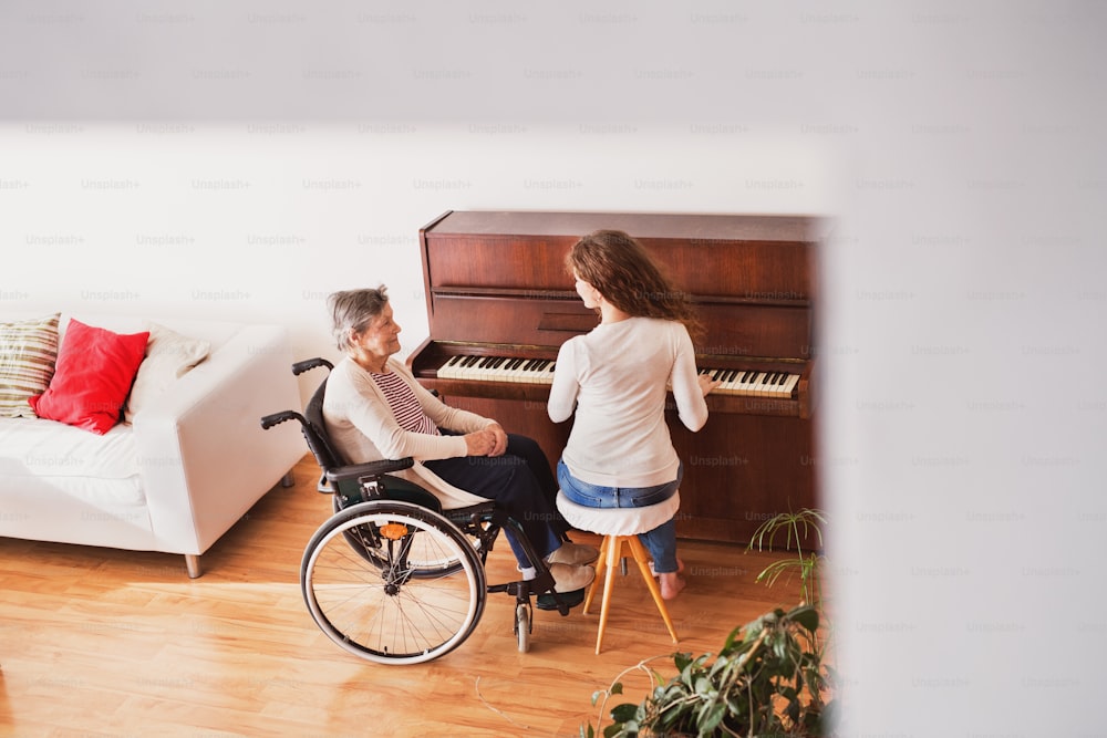 A teenage girl with grandmother in wheelchair playing the piano at home. Family and generations concept. High angle view.