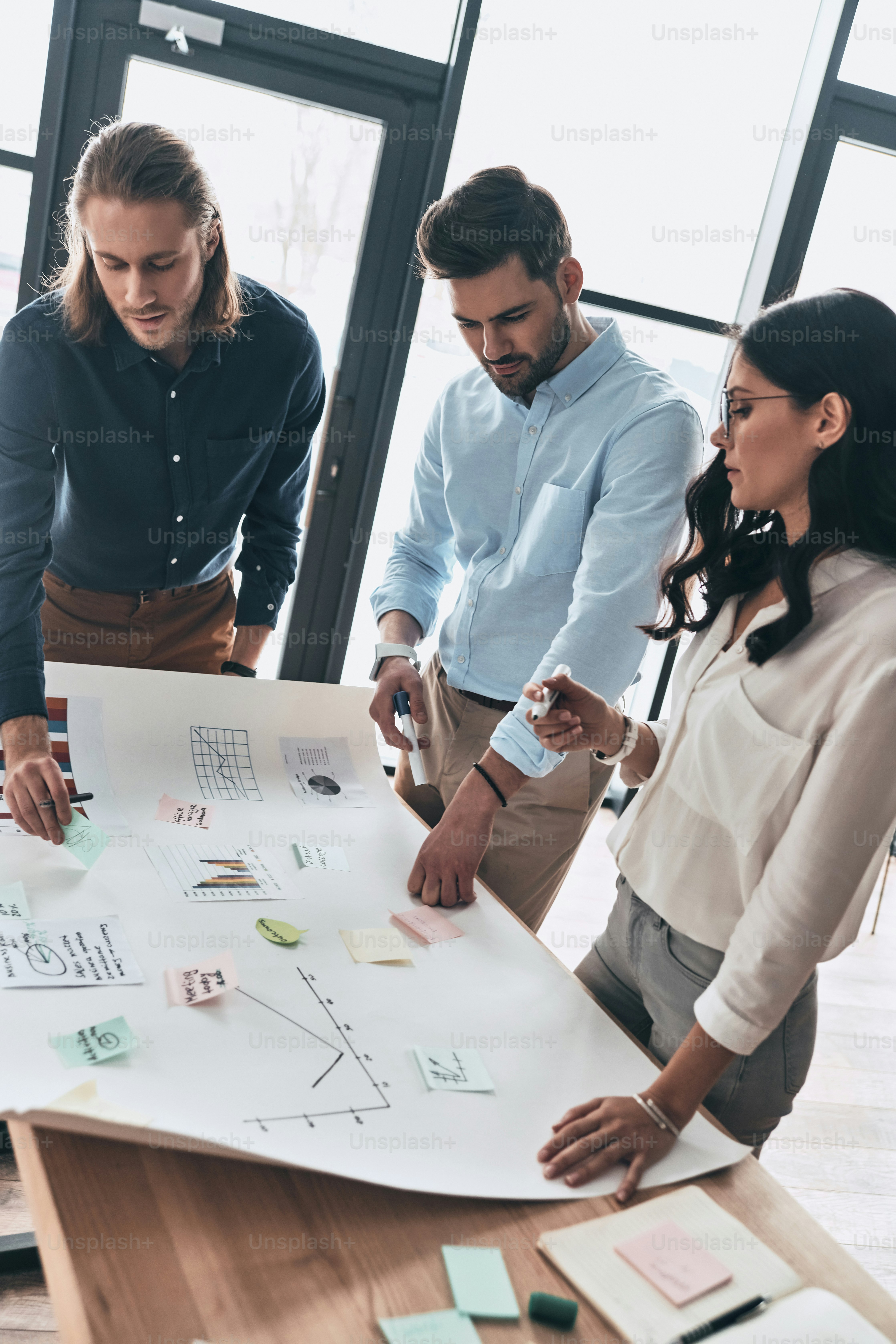 Top view of young confident business people discussing something while man writing on blueprint in the office