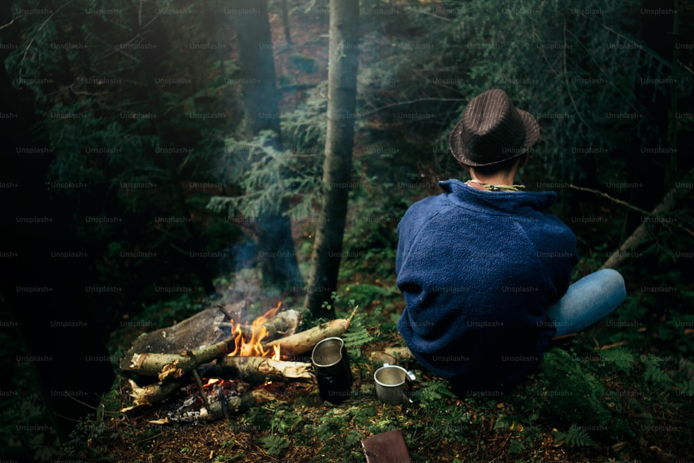 stylish hipster traveler camping in sunny forest in the mountains