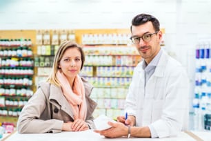 Portrait of handsome male friendly pharmacist with a female customer.