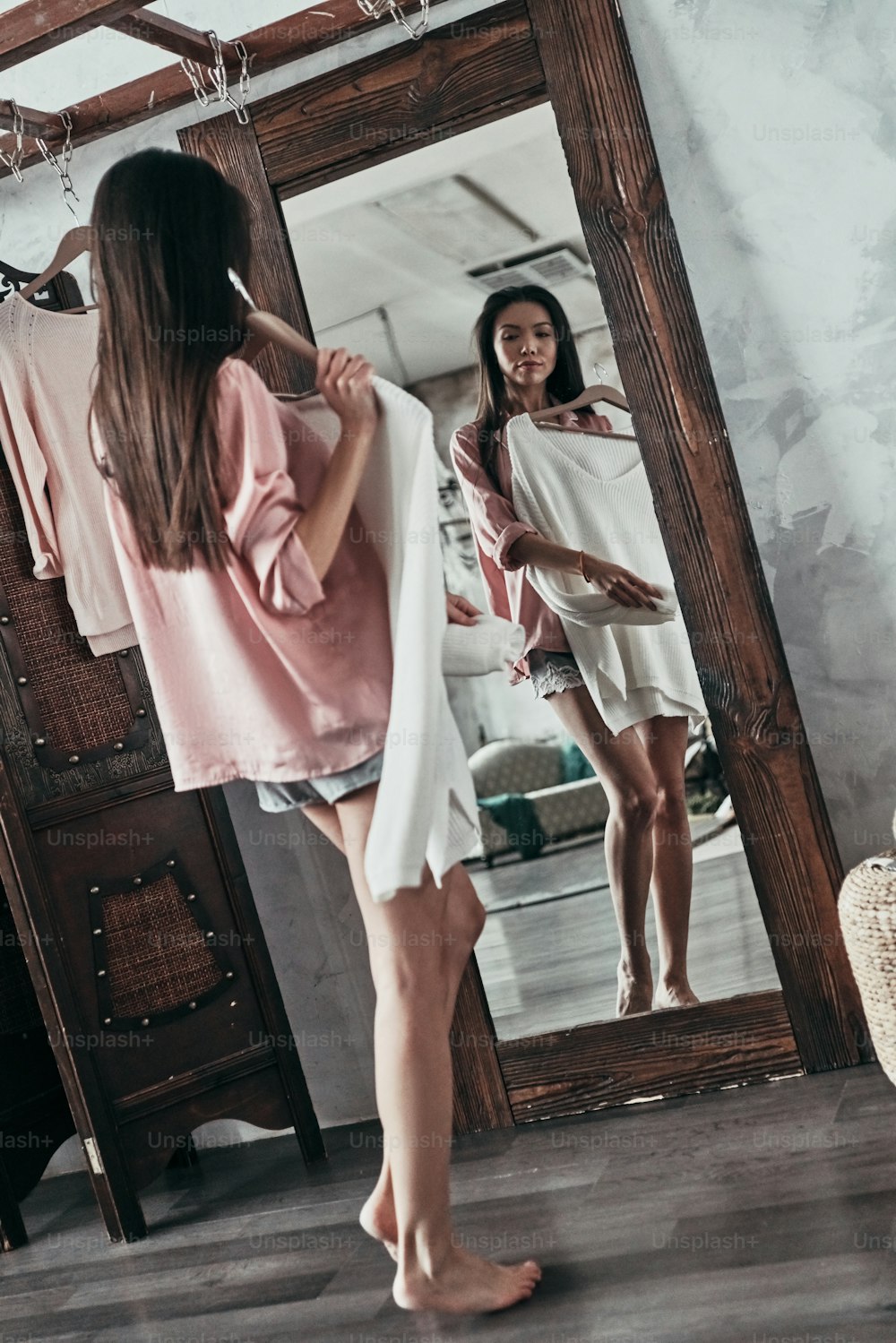 Comprimento total da mulher jovem atraente experimentando a blusa enquanto está em pé na frente do espelho em casa