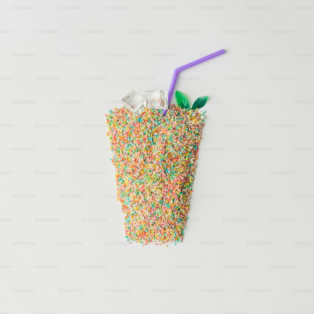 Verre à jus composé de paillettes de gâteau colorées avec des glaçons. Concept de boisson minimaliste créatif. Pose à plat.