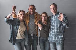 Portrait of four laughing people standing in embrace and demonstrating ok signs. Isolated on background
