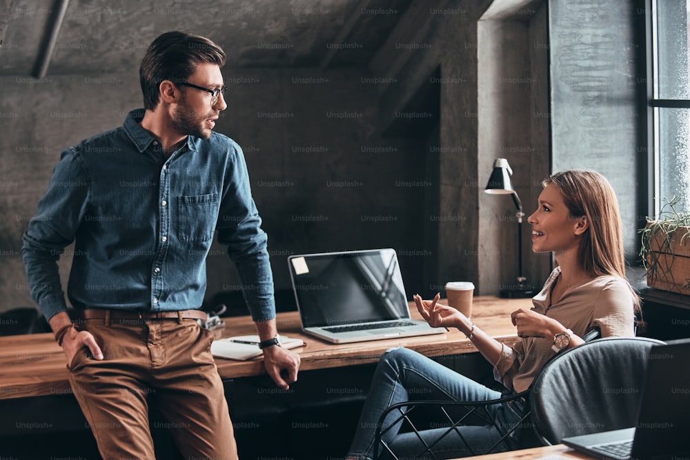 Des gens d’affaires confiants qui parlent et sourient tout en travaillant au bureau